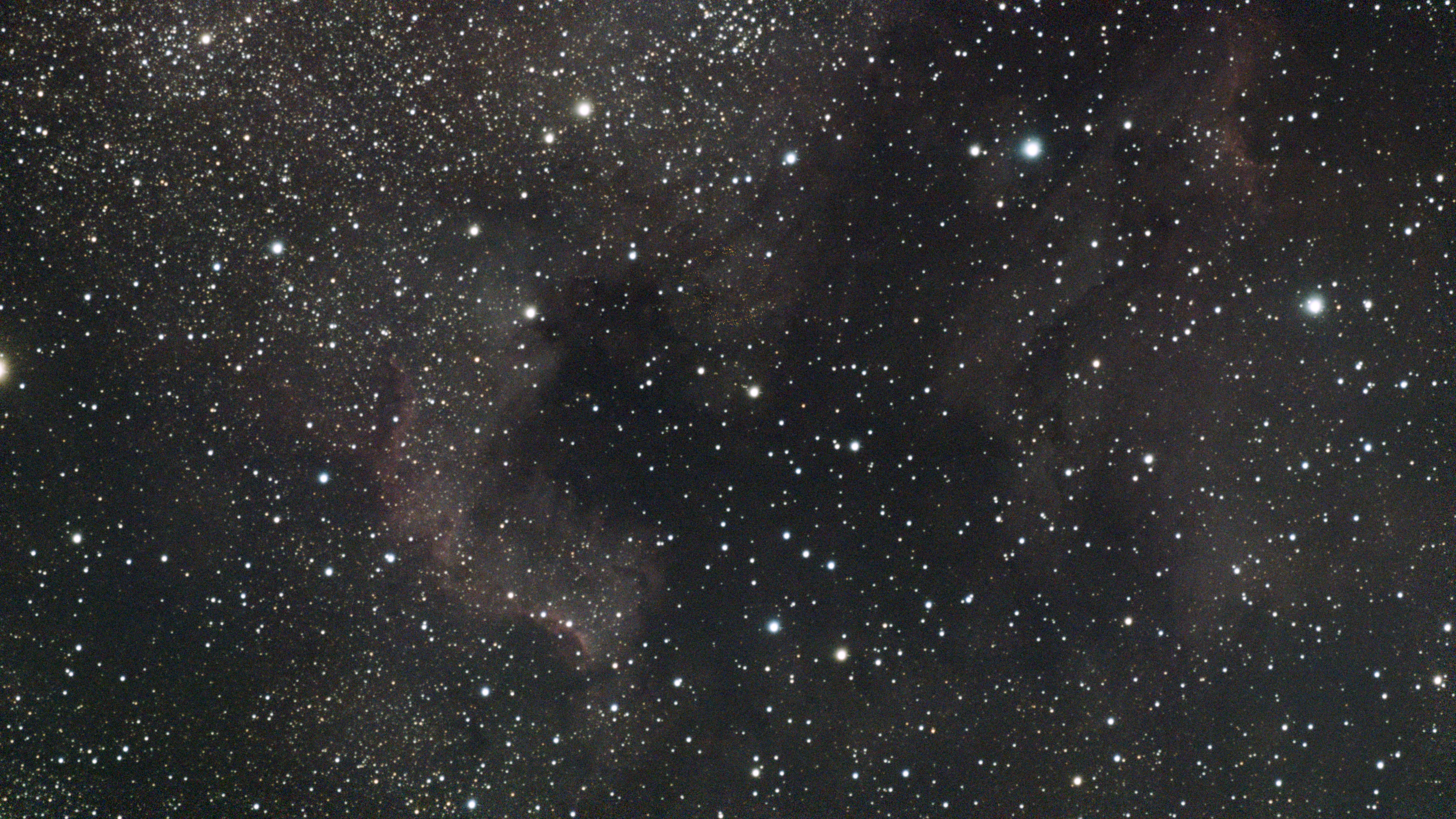 The dark dust lane LDN 935 between the faint red glow of the North America and Pelican Nebulae in a dense star field